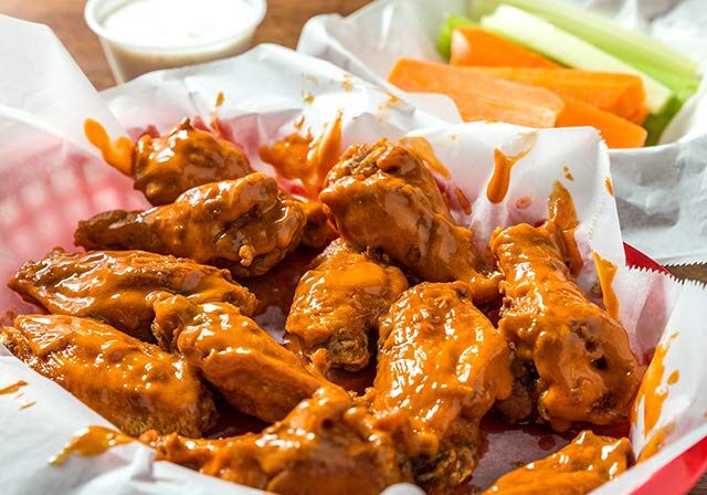 A basket of spicy buffalo chicken wings with celery and carrot sticks.